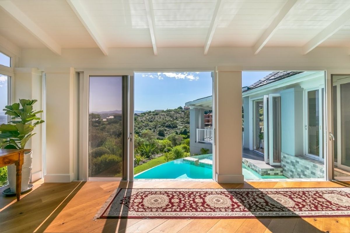 Bright living area featuring hardwood floors and exposed beam ceilings, opening directly onto a scenic patio with a swimming pool and landscape views.