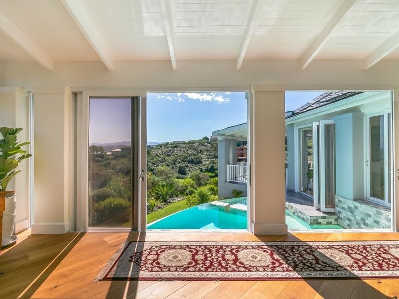 Bright living area featuring hardwood floors and exposed beam ceilings, opening directly onto a scenic patio with a swimming pool and landscape views.