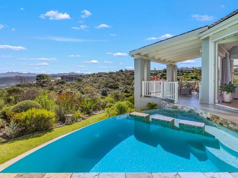 An inviting infinity edge swimming pool with integrated steps, adjacent to a covered patio area offering expansive scenic views.