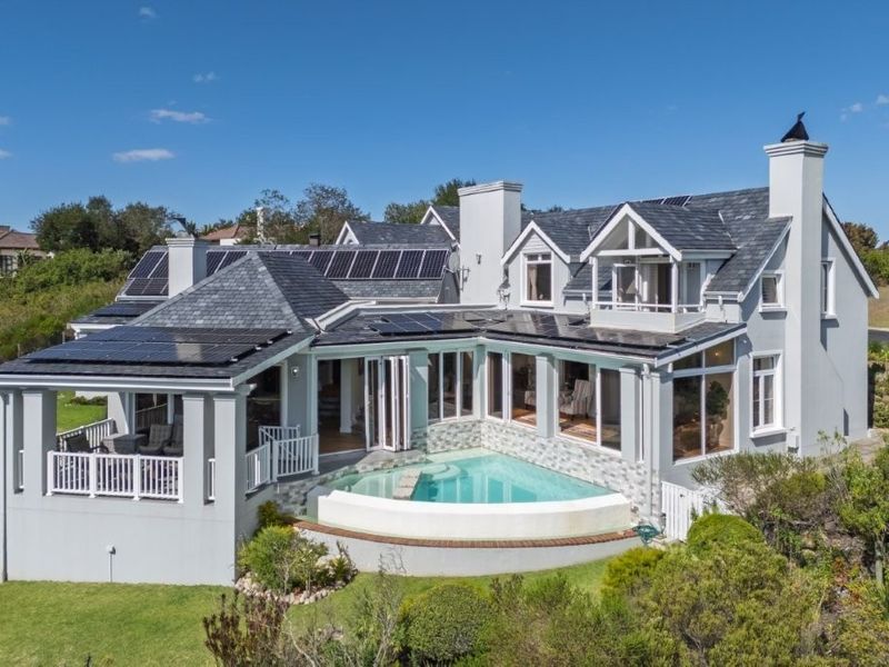 Aerial view of the rear elevation featuring a swimming pool, bi-fold doors, balcony, and extensive roof-mounted solar panel installation.