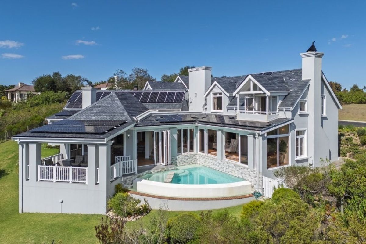 Aerial view of the rear elevation featuring a swimming pool, bi-fold doors, balcony, and extensive roof-mounted solar panel installation.