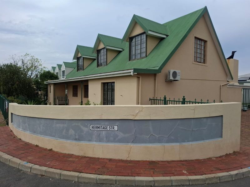 Street-facing view of a house featuring a green corrugated metal roof, dormer windows, and a perimeter boundary wall with visible plaster cracking.