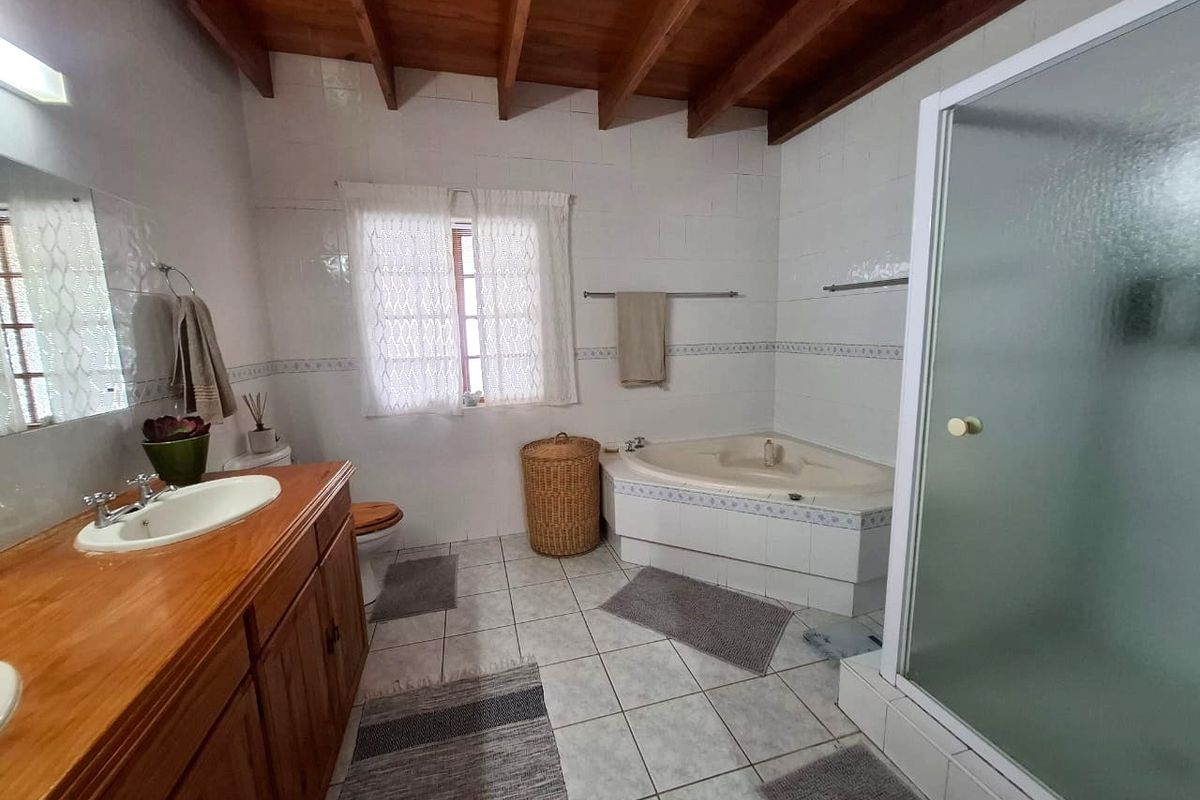 A functional bathroom featuring a corner bathtub, separate shower enclosure, wooden vanity cabinet, and exposed timber ceiling beams.