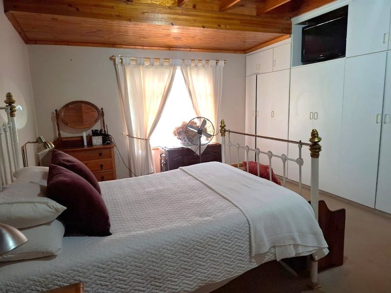 A cozy bedroom featuring a warm timber ceiling with exposed rafters and ample built-in cupboard storage.