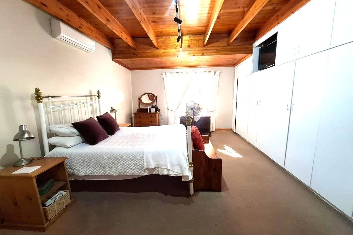Spacious bedroom featuring exposed timber ceiling beams, built-in floor-to-ceiling wardrobes, and a wall-mounted air conditioning unit.