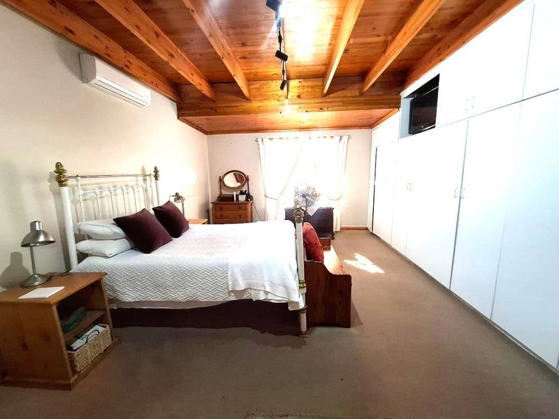 Spacious bedroom featuring exposed timber ceiling beams, built-in floor-to-ceiling wardrobes, and a wall-mounted air conditioning unit.
