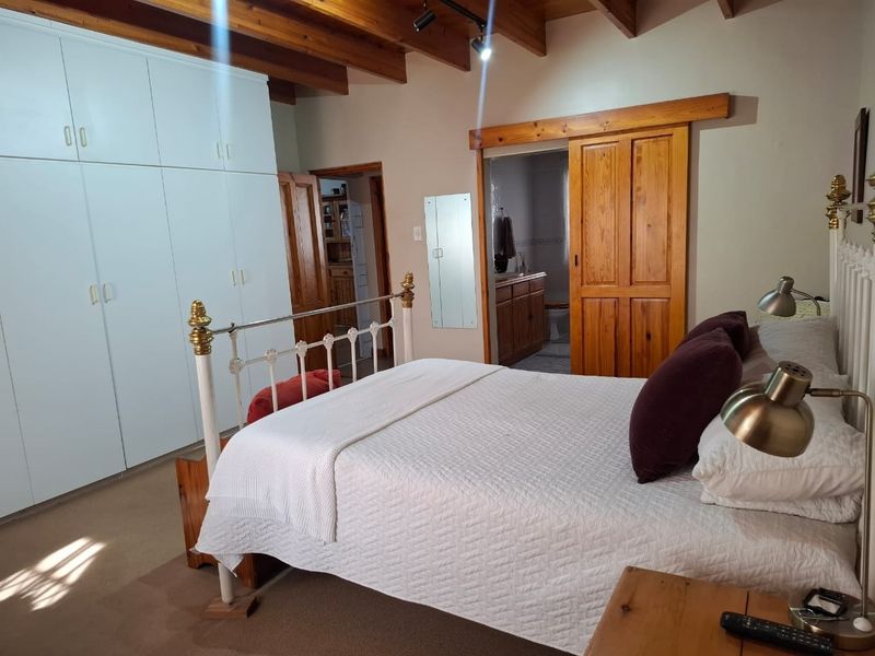 Spacious bedroom featuring exposed timber ceiling beams, extensive built-in cupboards, and a sliding timber door leading to an en-suite bathroom.