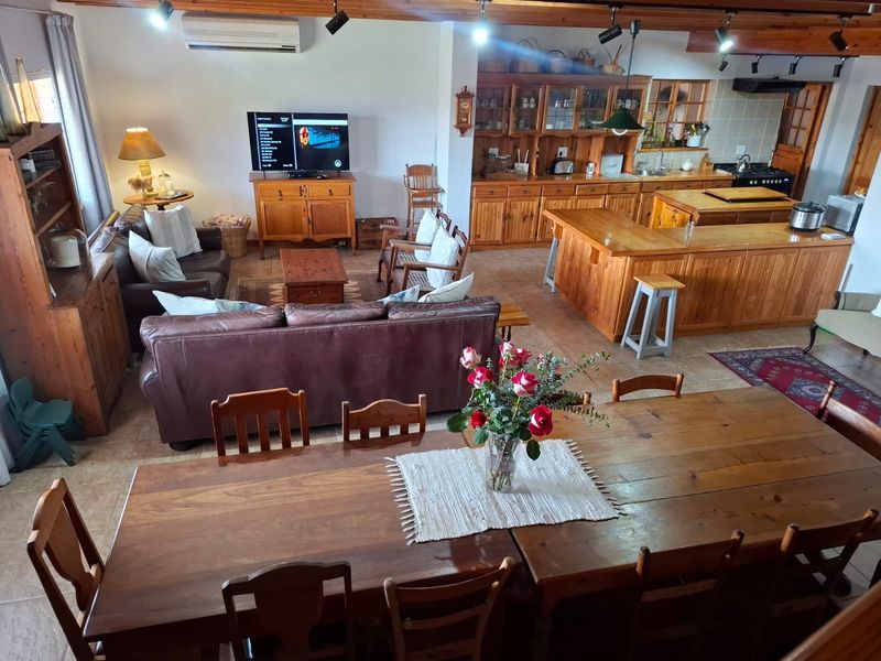 Spacious open-plan living, dining, and kitchen area featuring timber cabinetry, exposed ceiling beams, and a large central island, creating a warm, functional family space.