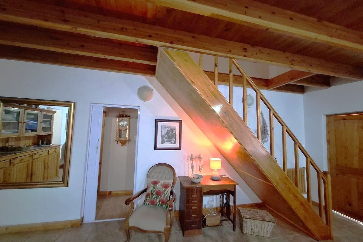 Living area featuring exposed timber ceiling beams, a wooden staircase with balustrade, and tiled flooring.