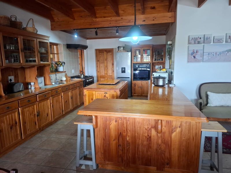 A spacious kitchen featuring extensive wooden cabinetry, a central island, exposed timber ceiling beams, and integrated appliances, offering a warm, traditional aesthetic.