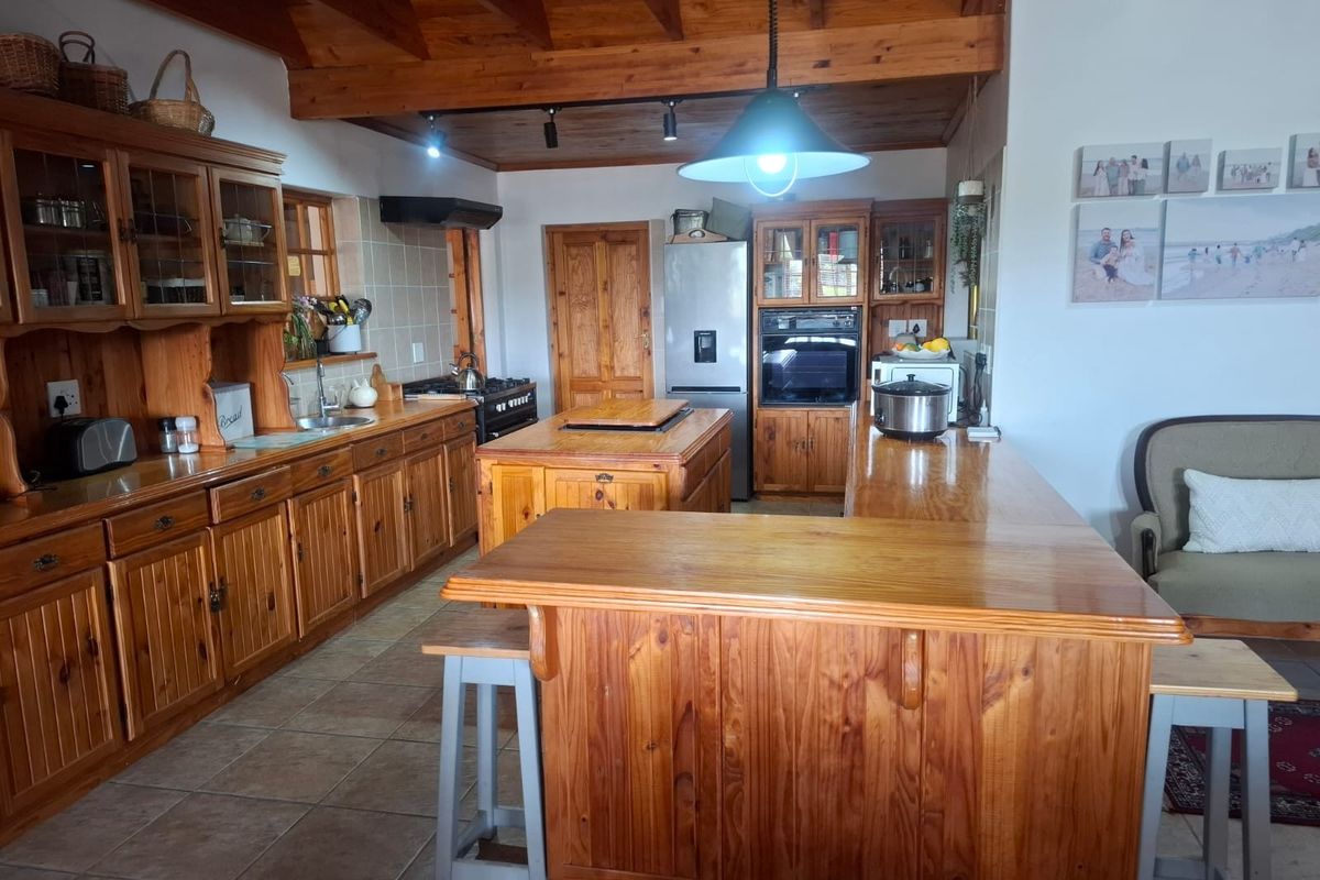 A spacious kitchen featuring extensive wooden cabinetry, a central island, exposed timber ceiling beams, and integrated appliances, offering a warm, traditional aesthetic.