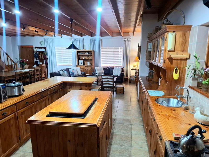 Spacious open-plan living and kitchen area featuring exposed timber ceiling beams, extensive timber cabinetry, and a central kitchen island with tiled flooring throughout.