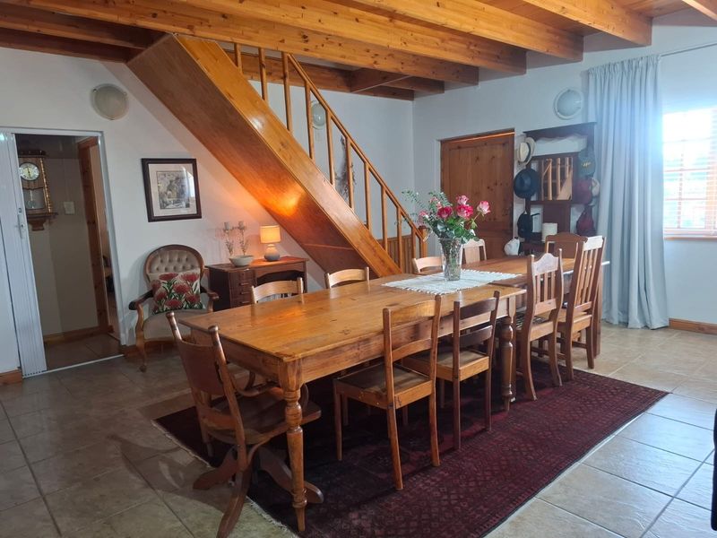 Dining area featuring exposed timber ceiling beams, tiled flooring, and a wooden staircase with a matching balustrade.