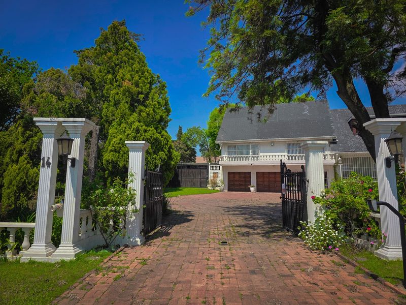 Front view of a two-story house featuring a brick-paved driveway, double garage, and decorative entrance pillars with wrought iron gates.