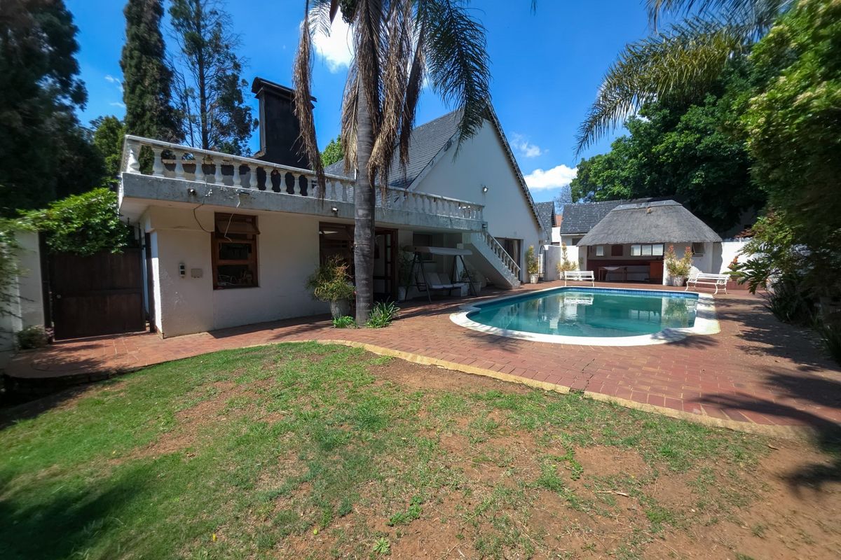 Rear garden view featuring a swimming pool, brick-paved patio area, and a detached thatched lapa structure.