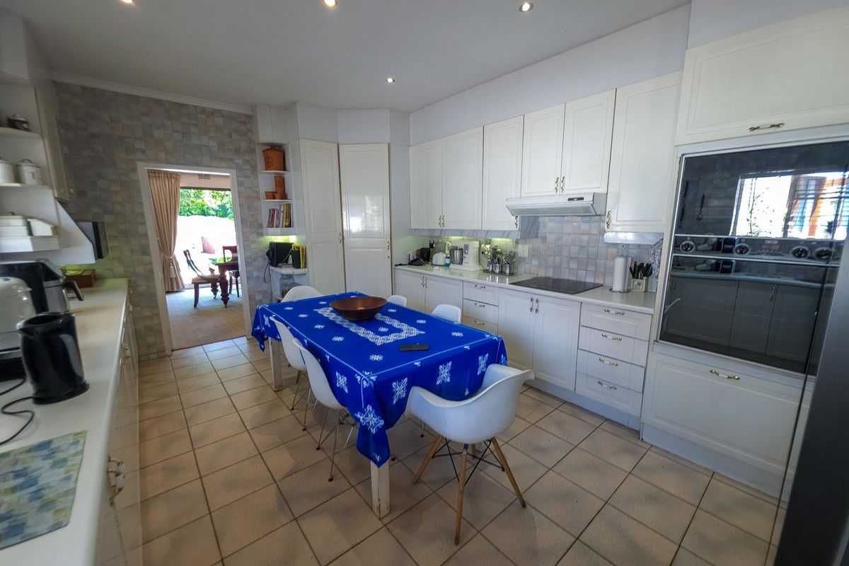 Spacious kitchen featuring white cabinetry, tiled flooring, built-in oven, and cooktop, with direct access to an adjoining living area.