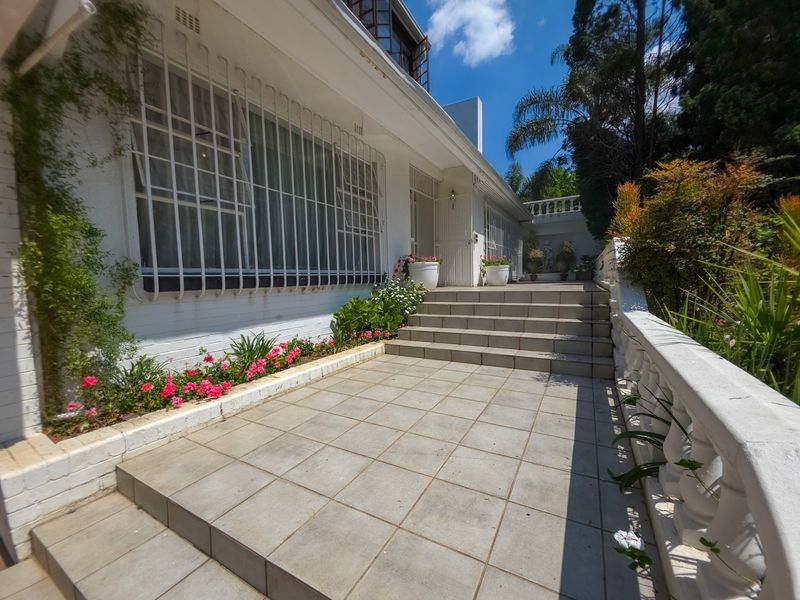 A well-maintained front entrance featuring tiled steps, a classic balustrade, and established garden beds leading to the main house facade.