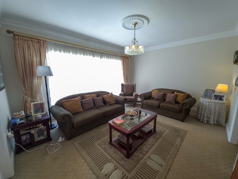 A traditional living room featuring a decorative ceiling rose, crystal chandelier, and wall-to-wall carpeting, offering a classic and comfortable space.