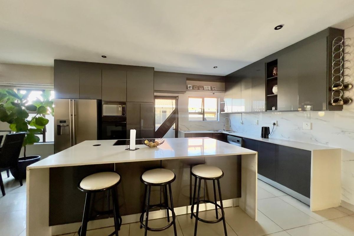 Modern kitchen featuring high-gloss cabinetry, a large central island with stone countertops, built-in appliances, and sleek tiled flooring.