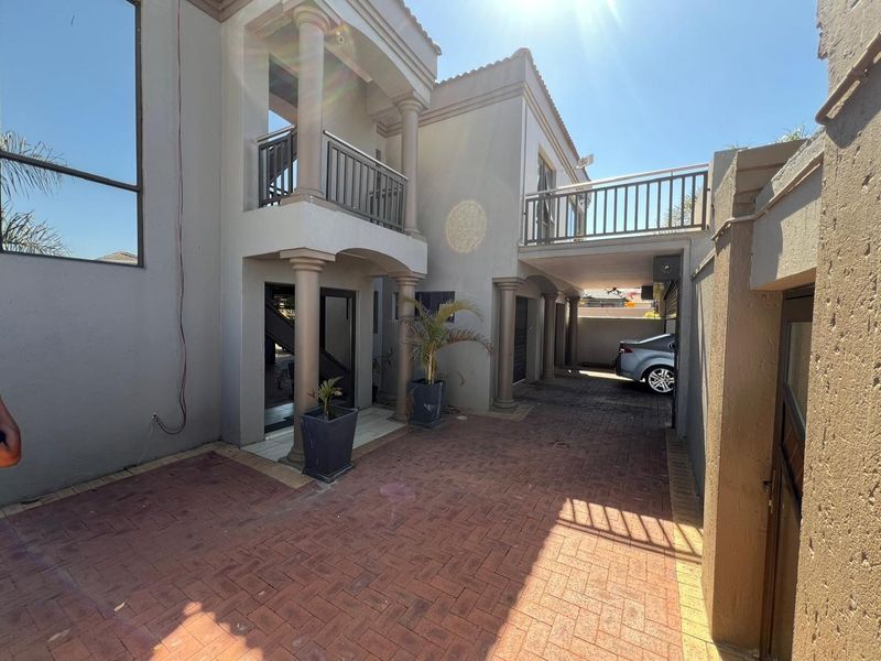 Rear exterior view featuring a paved driveway, covered patio area, and an upper-level balcony with metal railings.
