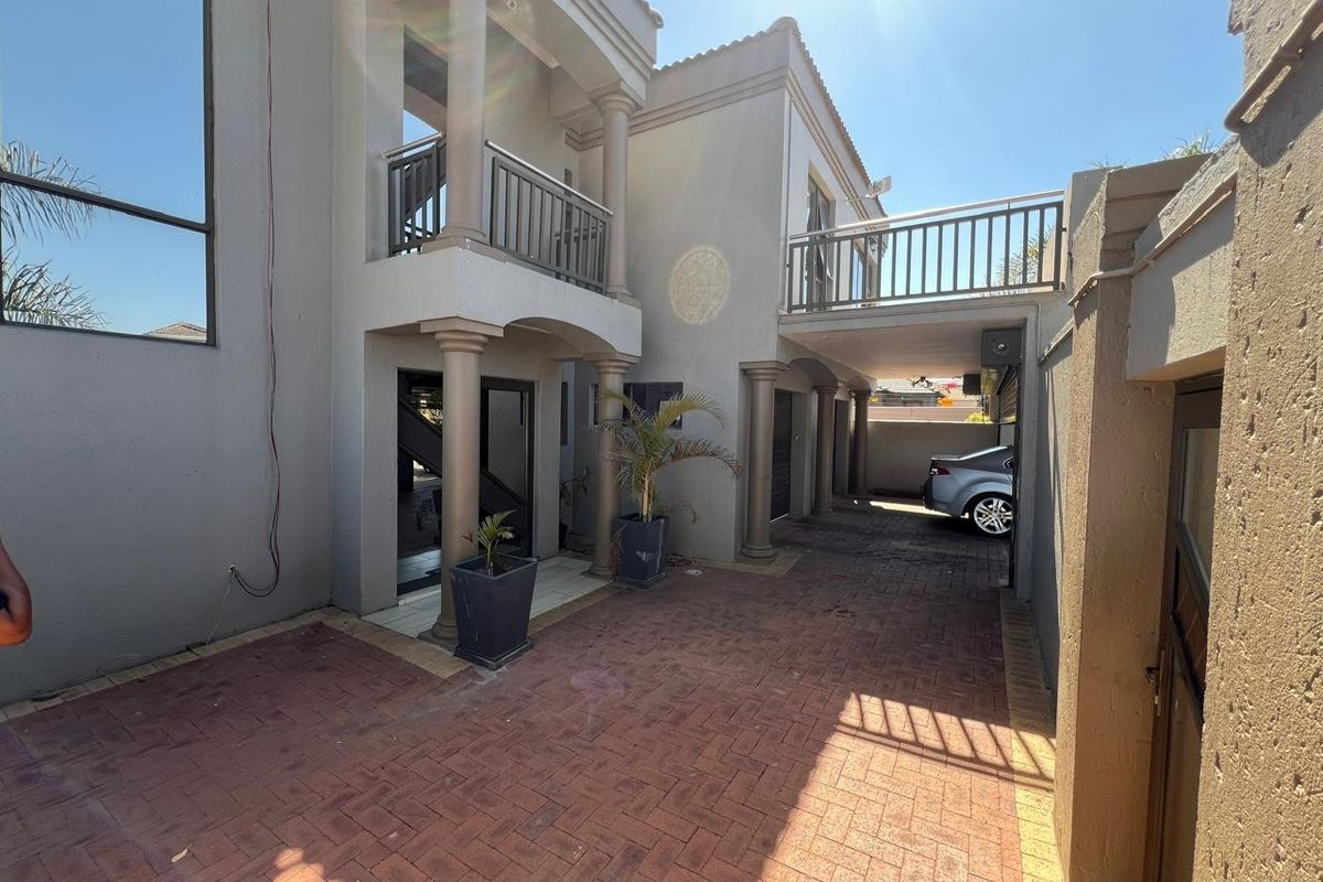 Rear exterior view featuring a paved driveway, covered patio area, and an upper-level balcony with metal railings.