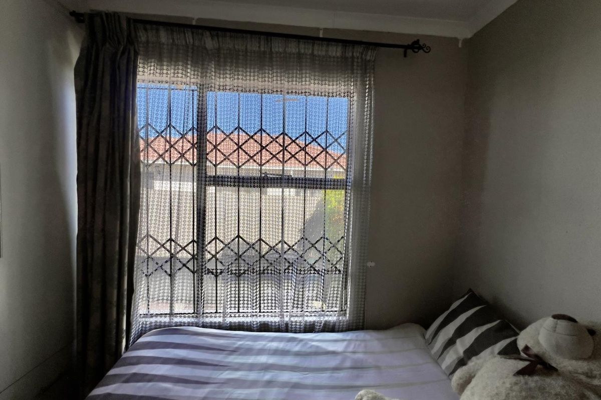A bedroom featuring a window with a fitted security gate and curtain rod, providing natural light and a view of the neighboring property.