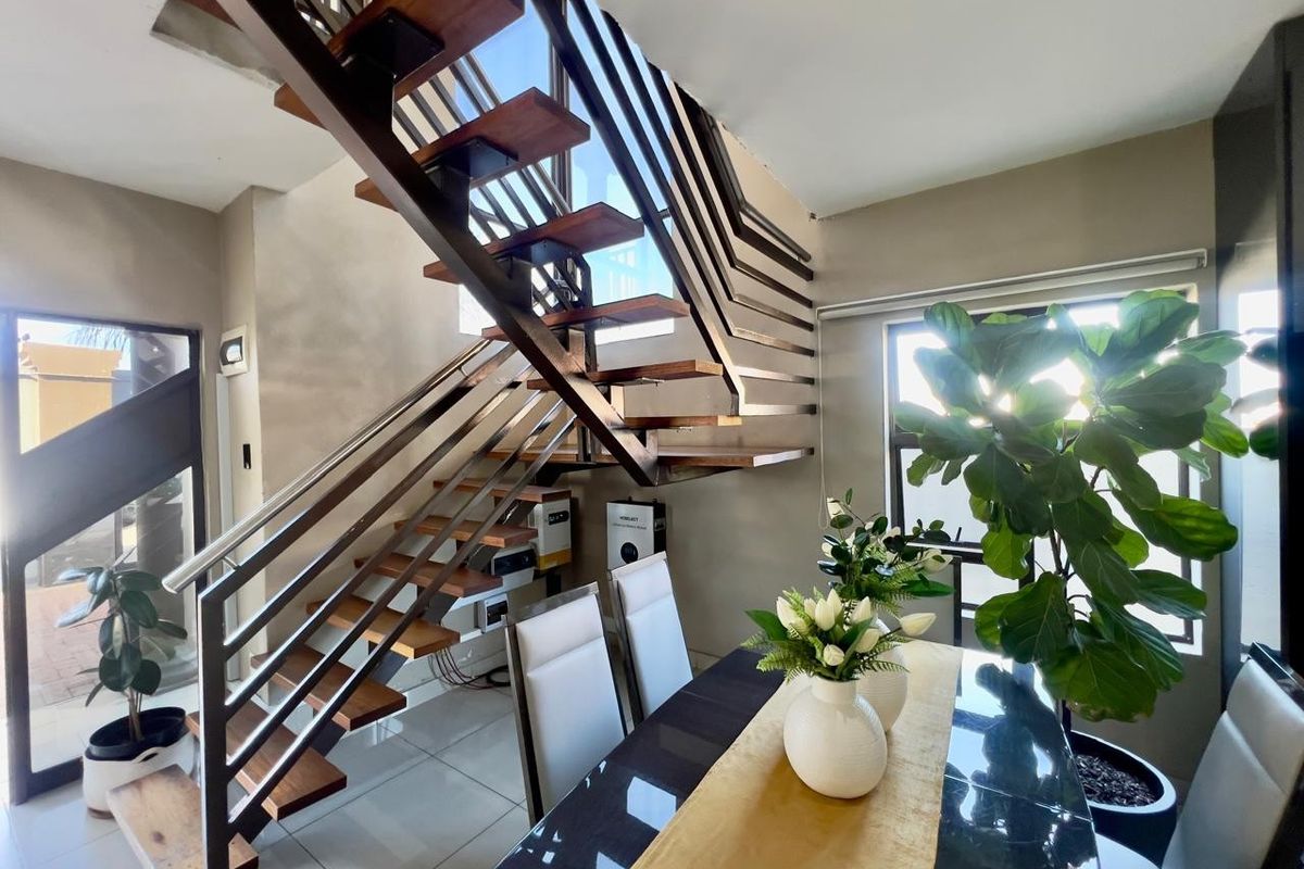 Modern living area featuring a striking open-tread staircase with metal balustrades, large windows for natural light, and sleek tiled flooring.