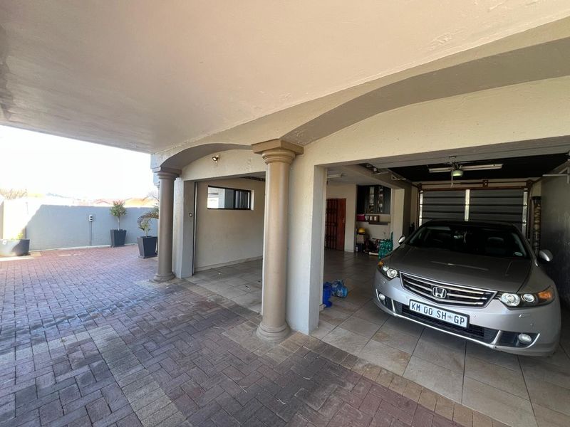 Spacious covered garage area with paved driveway, tiled flooring, and structural columns, providing ample parking space.