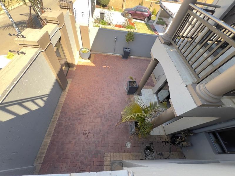 An elevated view of a paved rear courtyard area featuring boundary walls, drainage, and access to the upper balcony level.