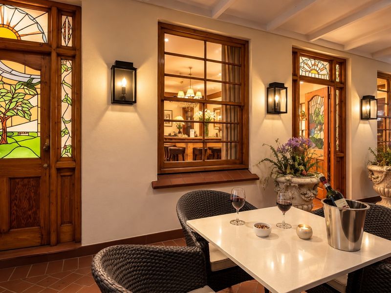A charming covered patio featuring terracotta flooring, exposed beam ceilings, and elegant stained glass timber doors, creating a warm and inviting outdoor entertainment space.