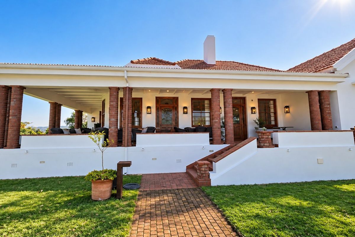 A well-maintained rear exterior view featuring a spacious covered patio with brick columns, terracotta roof tiles, and a paved walkway leading to the entrance.