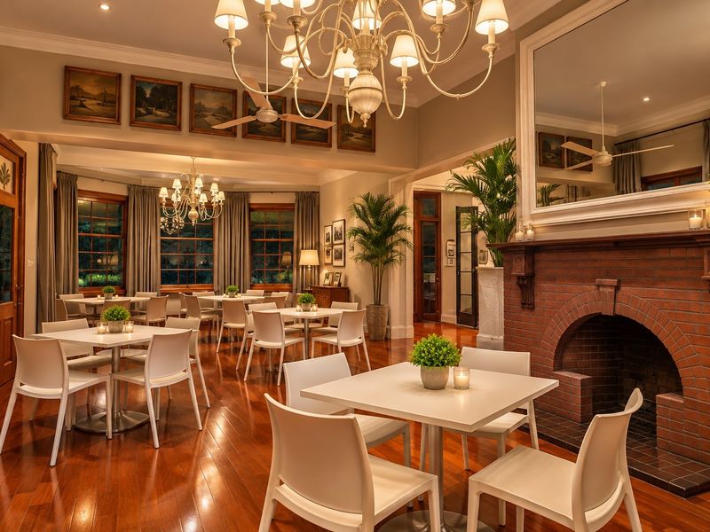 Spacious living area featuring polished hardwood floors, a classic brick fireplace, elegant chandeliers, and crown molding, creating a warm and inviting atmosphere.