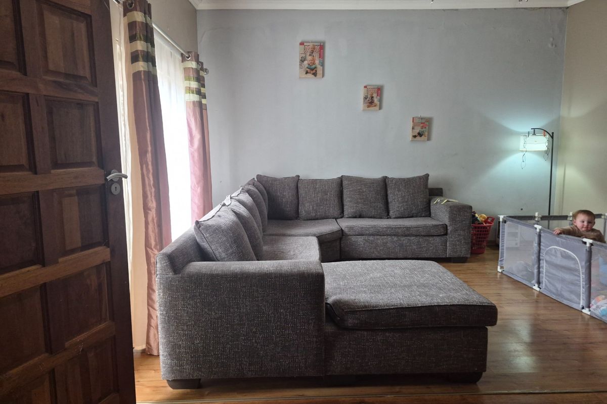 A living room featuring laminate flooring and a timber entrance door, requiring cosmetic updates to the wall finishes.