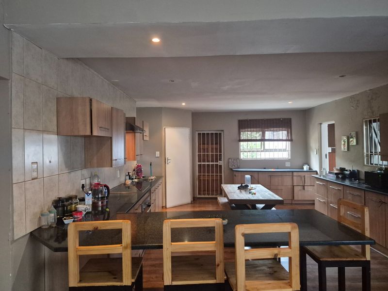 Open-plan kitchen and dining area featuring granite countertops, built-in cabinetry, and recessed lighting, with some visible wall surface wear requiring maintenance.