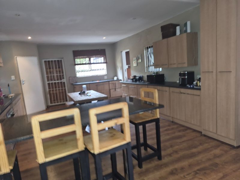 A functional kitchen featuring light wood cabinetry, dark laminate countertops, and laminate flooring, with an integrated breakfast bar area.