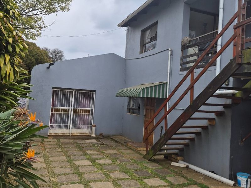 Rear exterior view of the property featuring a paved patio area, external timber staircase, and security gate access.