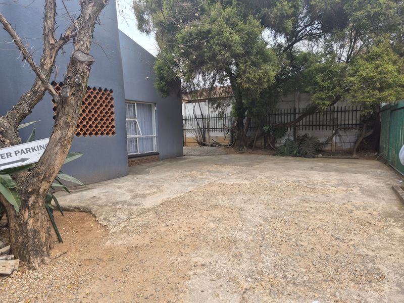 A rear exterior area featuring a concrete driveway, breeze block detailing, and perimeter steel security fencing.