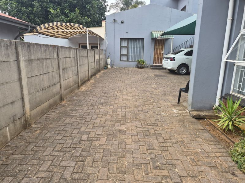 Rear exterior area featuring a paved driveway, precast concrete boundary wall, and covered access points to the main building structure.