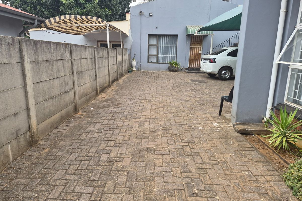 Rear exterior area featuring a paved driveway, precast concrete boundary wall, and covered access points to the main building structure.