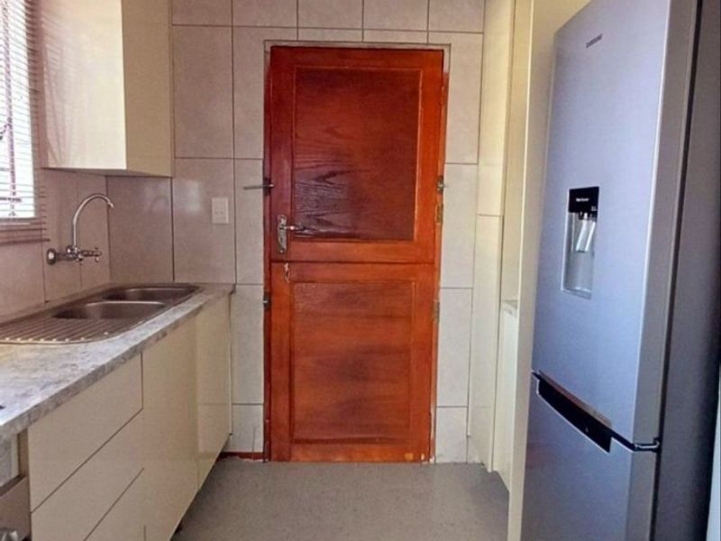 A functional galley-style kitchen featuring built-in cabinetry, laminate countertops, a double sink, and tiled splashbacks with a direct exterior access door.