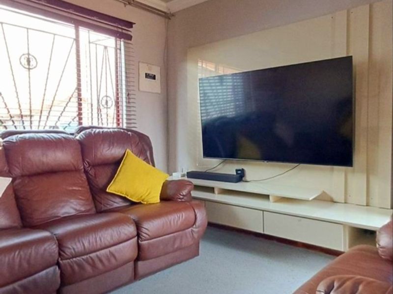 A comfortable living room featuring a built-in media console, recessed ceiling lighting, and security bars on the window.