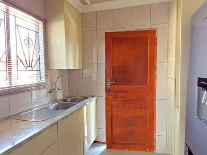 Functional scullery area featuring a double stainless steel sink, tiled splashback, and built-in cabinetry with direct access to the exterior.