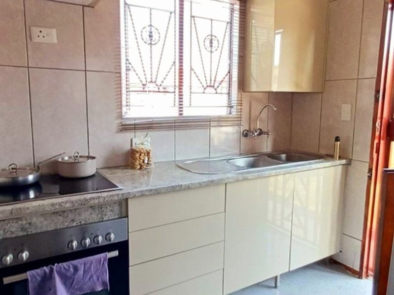 A functional kitchen featuring built-in cabinetry, a laminate countertop, stainless steel sink, and a built-in electric stove and oven with tiled splashbacks.