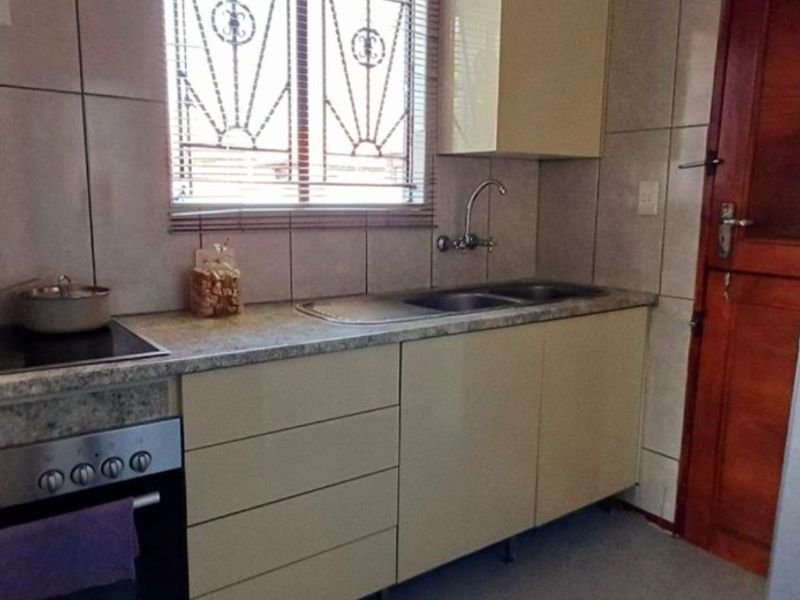 Functional kitchen featuring built-in cabinetry, laminate countertops, a stainless steel sink, and integrated oven with electric hob, finished with tiled walls.