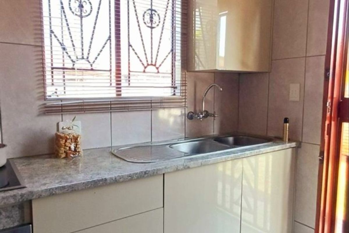 A functional kitchen featuring modern high-gloss cabinetry, a stainless steel sink, built-in oven, and tiled finishes with natural light from the window.