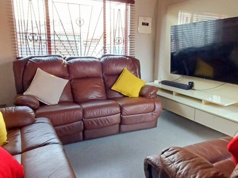 A comfortable living room featuring a built-in media console, recessed ceiling lighting, and windows fitted with security bars and venetian blinds.