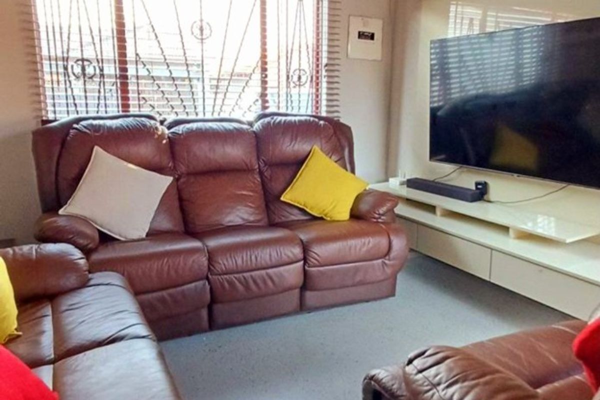 A comfortable living room featuring a built-in media console, recessed ceiling lighting, and windows fitted with security bars and venetian blinds.
