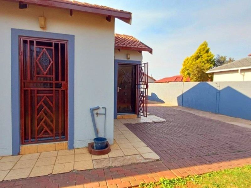Rear exterior view of the property featuring a paved driveway, security gates, and a boundary wall.