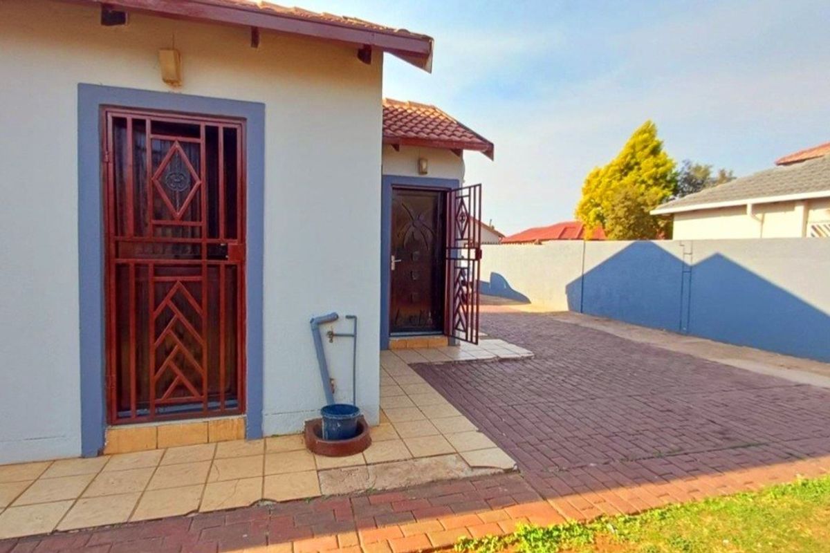 Rear exterior view of the property featuring a paved driveway, security gates, and a boundary wall.