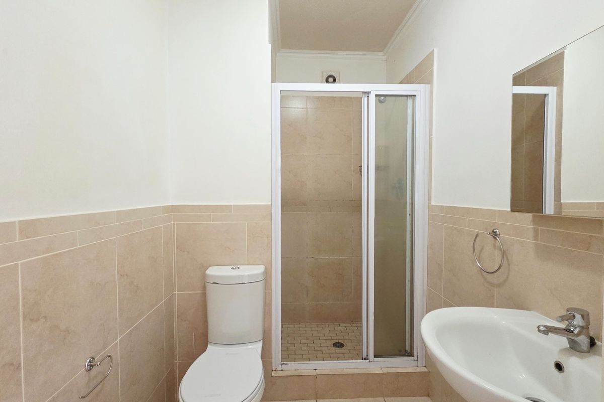 A functional bathroom featuring a shower enclosure, toilet, and washbasin with neutral wall tiling and tiled flooring.